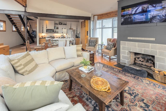 living area with stairs, lofted ceiling, light wood-style flooring, and a fireplace