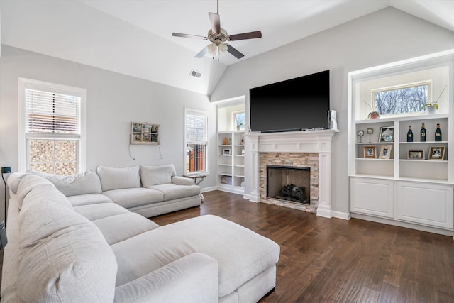 living area with visible vents, vaulted ceiling, a stone fireplace, dark wood-style floors, and a ceiling fan