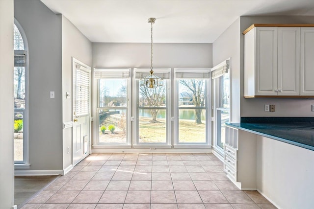 unfurnished dining area with a wealth of natural light, baseboards, an inviting chandelier, and light tile patterned floors