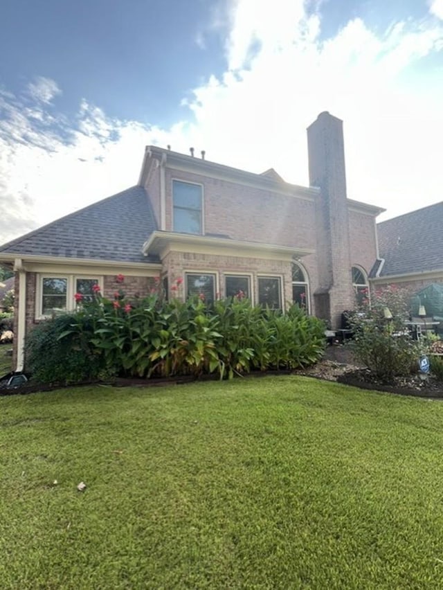 exterior space with a front lawn, a chimney, brick siding, and a shingled roof