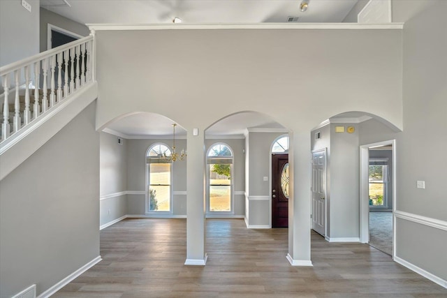 foyer with crown molding, a high ceiling, wood finished floors, and arched walkways