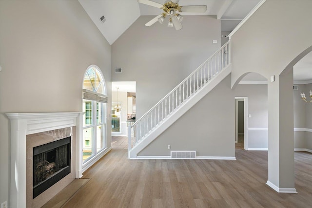 unfurnished living room with wood finished floors, a ceiling fan, visible vents, and arched walkways