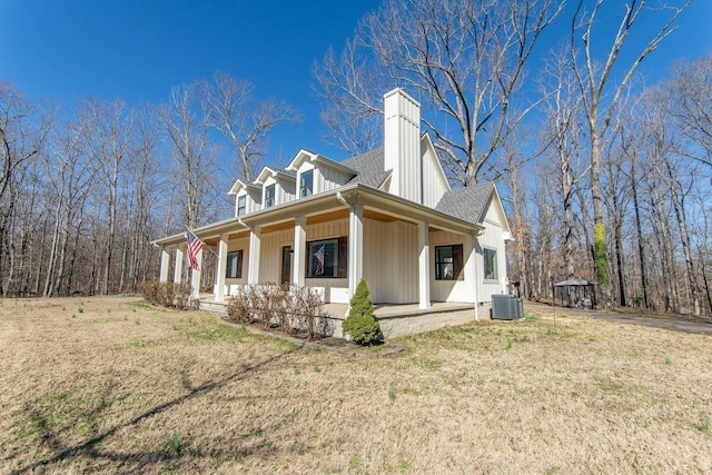 view of front of home featuring a front lawn, a porch, central AC, roof with shingles, and a chimney