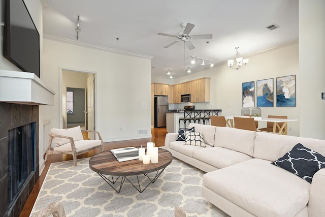 living room with visible vents, ceiling fan with notable chandelier, wood finished floors, a fireplace, and crown molding