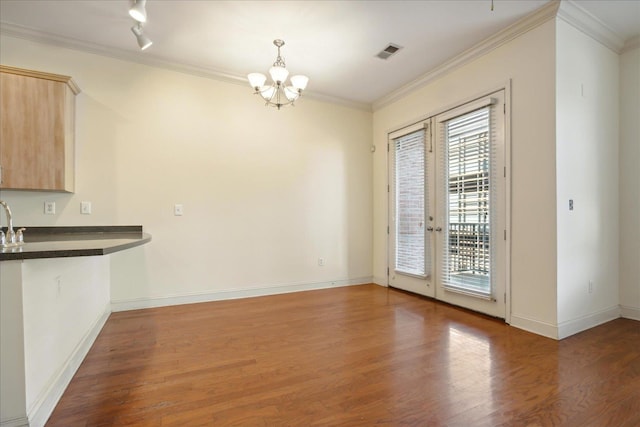 unfurnished dining area featuring a notable chandelier, wood finished floors, french doors, crown molding, and baseboards