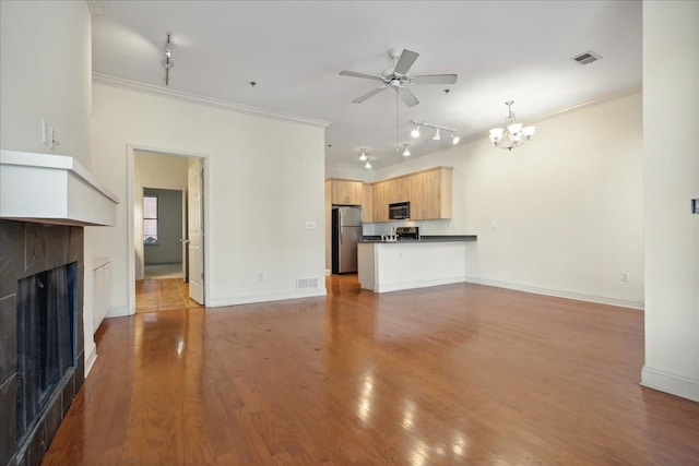 unfurnished living room featuring visible vents, a tiled fireplace, ornamental molding, ceiling fan with notable chandelier, and wood finished floors