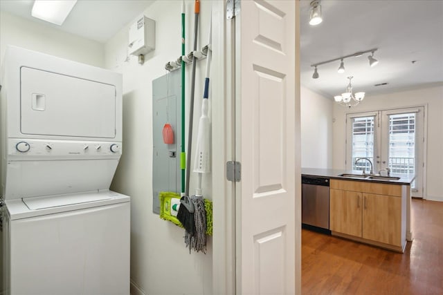 clothes washing area with track lighting, stacked washer and dryer, wood finished floors, a notable chandelier, and a sink