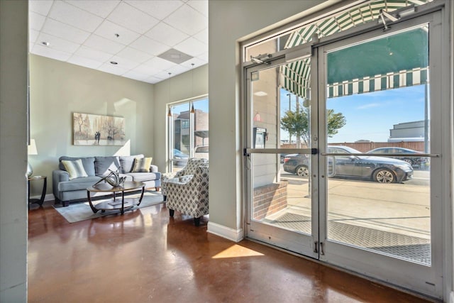 doorway with a drop ceiling, baseboards, and concrete flooring