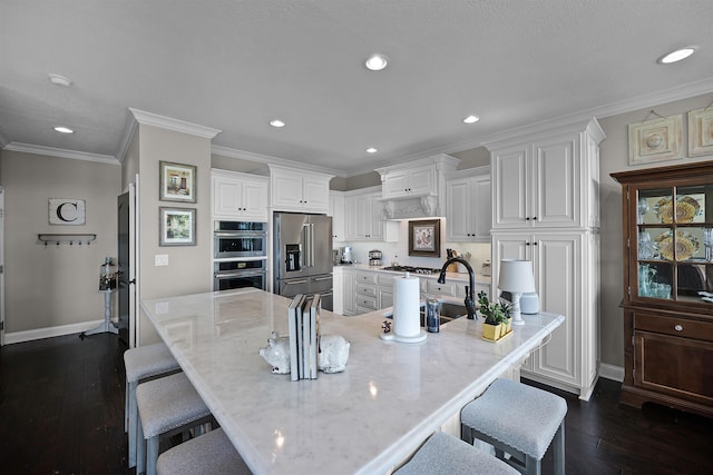 kitchen featuring dark wood-style flooring, a sink, stainless steel appliances, white cabinetry, and a kitchen bar