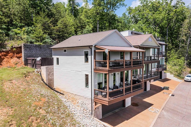 rear view of house featuring a balcony, roof with shingles, and fence