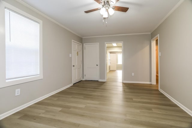 empty room featuring ceiling fan, baseboards, crown molding, and light wood-style floors