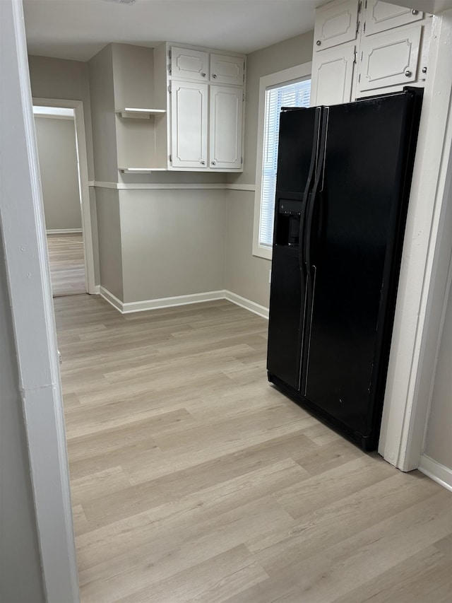 kitchen with light wood finished floors, black fridge with ice dispenser, white cabinetry, and baseboards