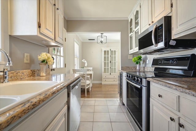 kitchen with glass insert cabinets, crown molding, light tile patterned floors, stainless steel appliances, and a sink