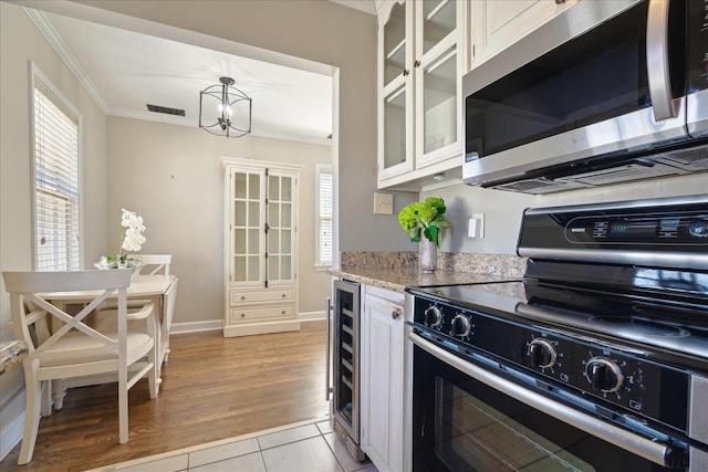 kitchen with ornamental molding, light stone counters, wine cooler, appliances with stainless steel finishes, and glass insert cabinets