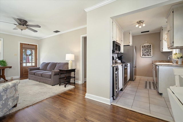 living room featuring visible vents, crown molding, baseboards, ceiling fan, and light wood-style flooring