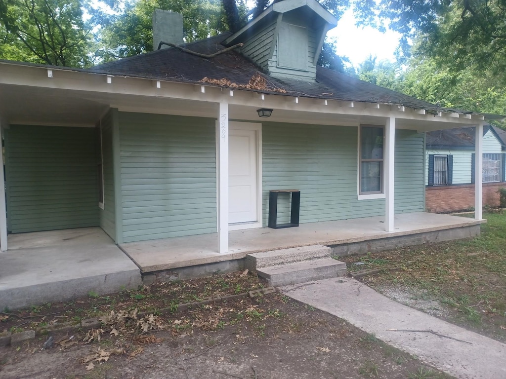 back of house with roof with shingles, covered porch, and a chimney