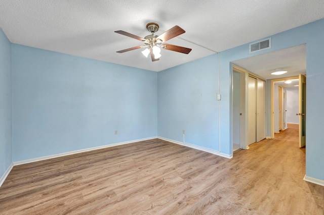 empty room with light wood-type flooring, visible vents, a ceiling fan, a textured ceiling, and baseboards