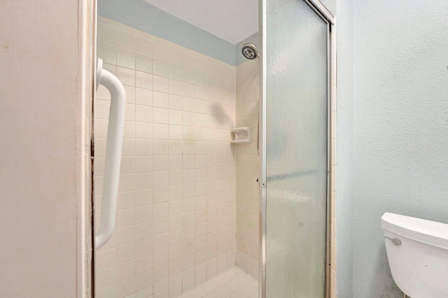 bathroom featuring a shower stall, toilet, and a textured wall