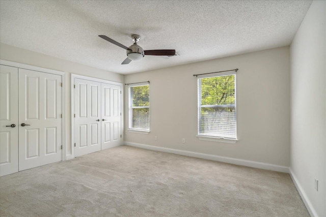 unfurnished bedroom with a textured ceiling, baseboards, two closets, and carpet floors