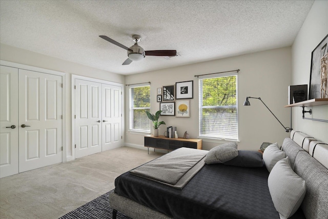 carpeted bedroom featuring a textured ceiling, multiple windows, multiple closets, and ceiling fan