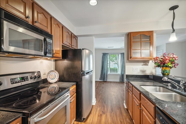 kitchen featuring dark stone countertops, brown cabinets, appliances with stainless steel finishes, wood finished floors, and a sink