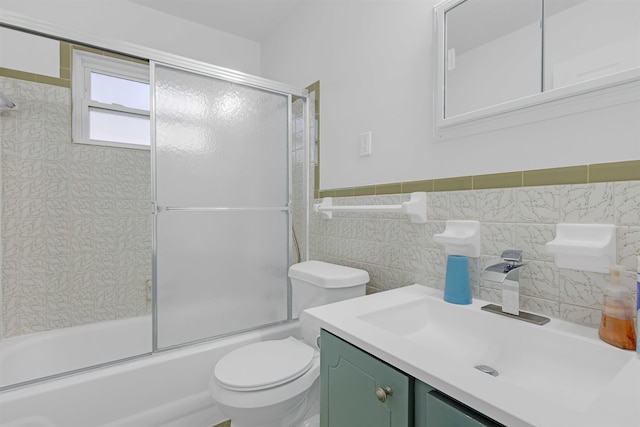 bathroom with vanity, shower / bath combination with glass door, wainscoting, tile walls, and toilet