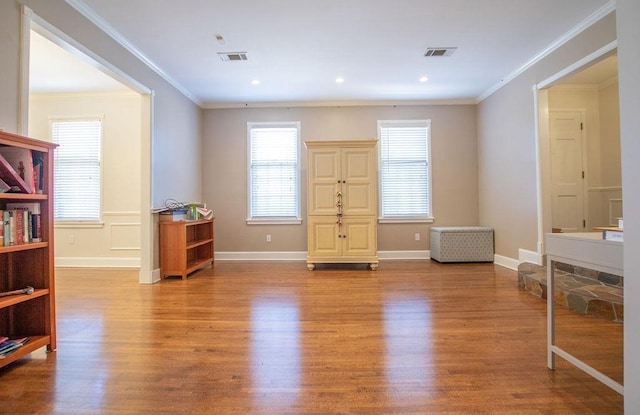 interior space with crown molding, wood finished floors, visible vents, and baseboards