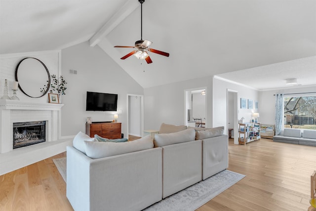 living room with beamed ceiling, visible vents, ceiling fan, light wood-style floors, and a brick fireplace