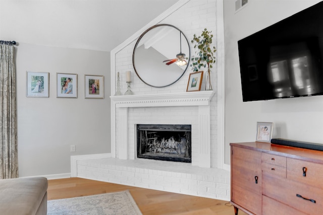 living area featuring a fireplace, lofted ceiling, wood finished floors, and visible vents