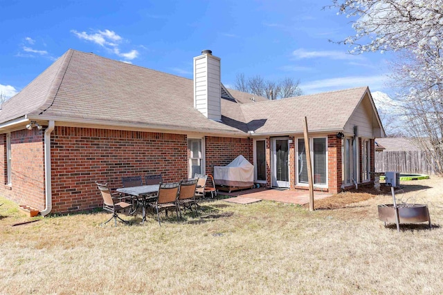 rear view of property featuring a patio area, brick siding, a chimney, and a lawn