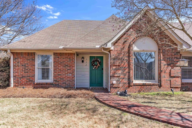 view of front of home with brick siding, roof with shingles, and a front yard