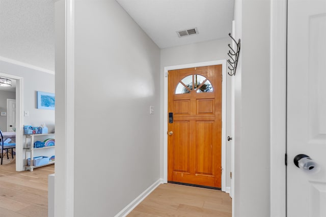 foyer entrance featuring visible vents, baseboards, a textured ceiling, and light wood-style flooring