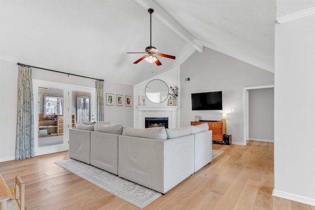 living room featuring beamed ceiling, a ceiling fan, light wood-style floors, a fireplace, and baseboards