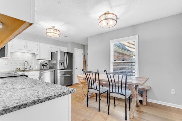 kitchen featuring light wood-type flooring, a sink, white cabinetry, stainless steel appliances, and decorative backsplash