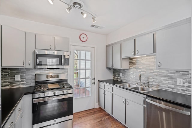 kitchen featuring visible vents, light wood finished floors, a sink, stainless steel appliances, and dark countertops