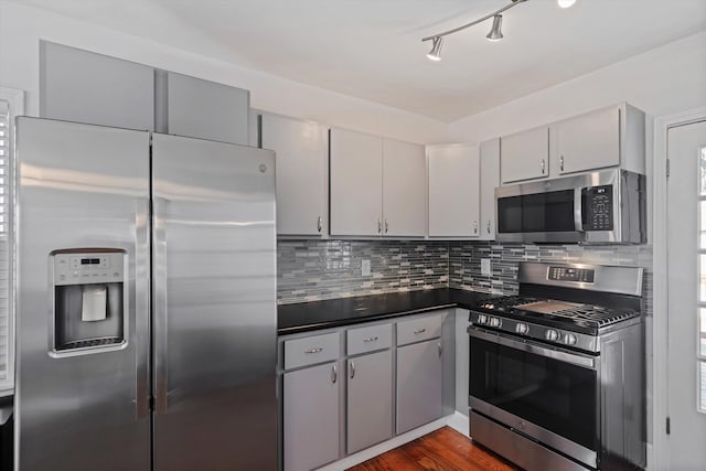 kitchen with dark countertops, tasteful backsplash, dark wood-type flooring, gray cabinets, and appliances with stainless steel finishes