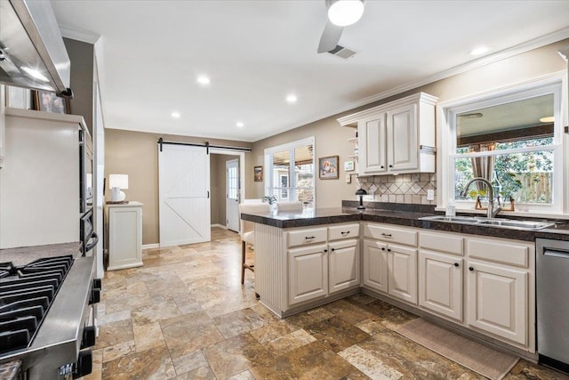 kitchen with a peninsula, a sink, stainless steel dishwasher, a barn door, and tasteful backsplash