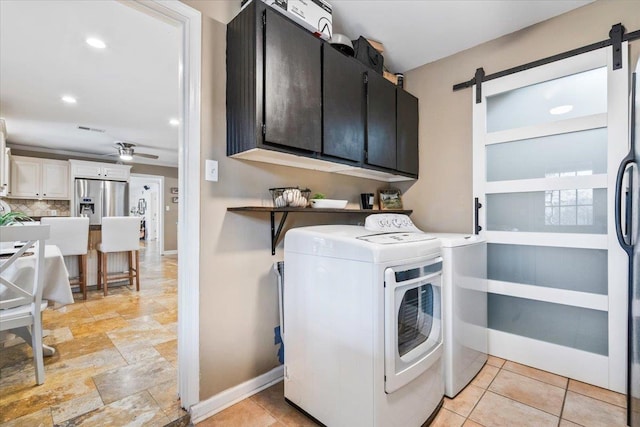 washroom featuring baseboards, ceiling fan, a barn door, cabinet space, and separate washer and dryer