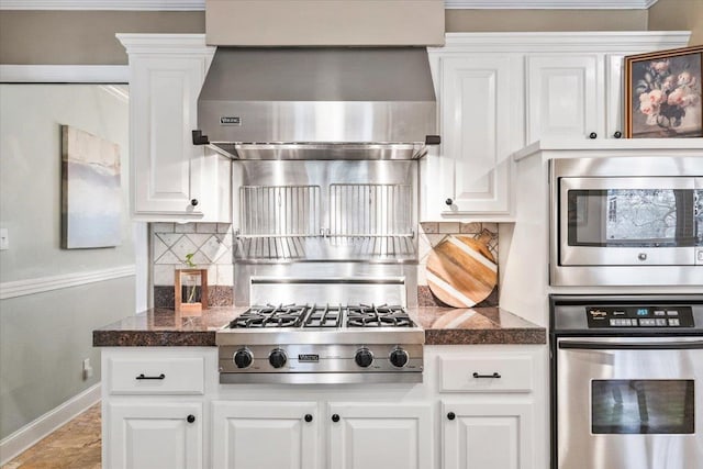 kitchen featuring tasteful backsplash, white cabinetry, tile countertops, stainless steel appliances, and wall chimney range hood