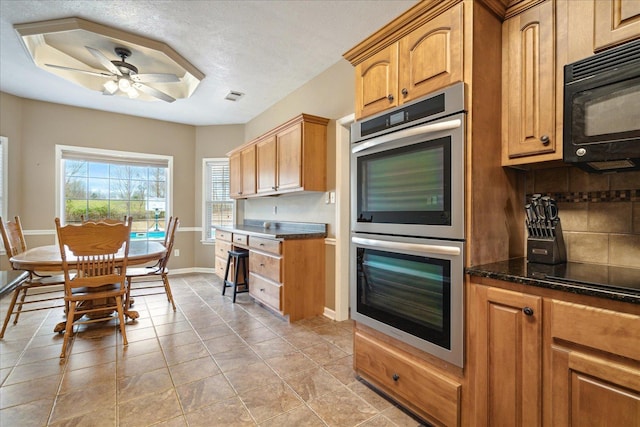 kitchen with a ceiling fan, visible vents, baseboards, decorative backsplash, and black appliances