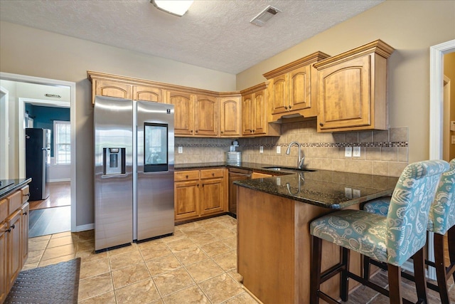 kitchen featuring a sink, tasteful backsplash, freestanding refrigerator, stainless steel fridge, and a peninsula