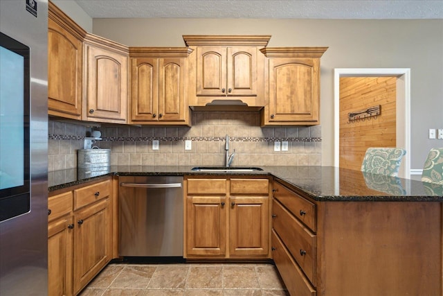 kitchen with backsplash, dark stone counters, appliances with stainless steel finishes, a peninsula, and a sink