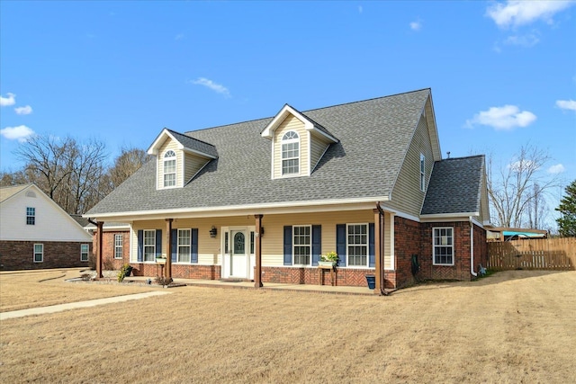 cape cod-style house featuring a porch, brick siding, roof with shingles, and fence