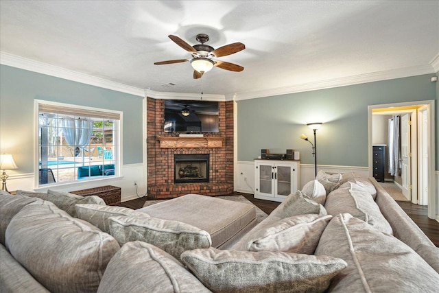 living room with wood finished floors, a wainscoted wall, a ceiling fan, a fireplace, and ornamental molding