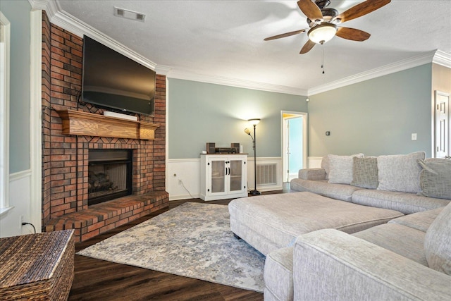 living area featuring a ceiling fan, wood finished floors, a wainscoted wall, ornamental molding, and a brick fireplace