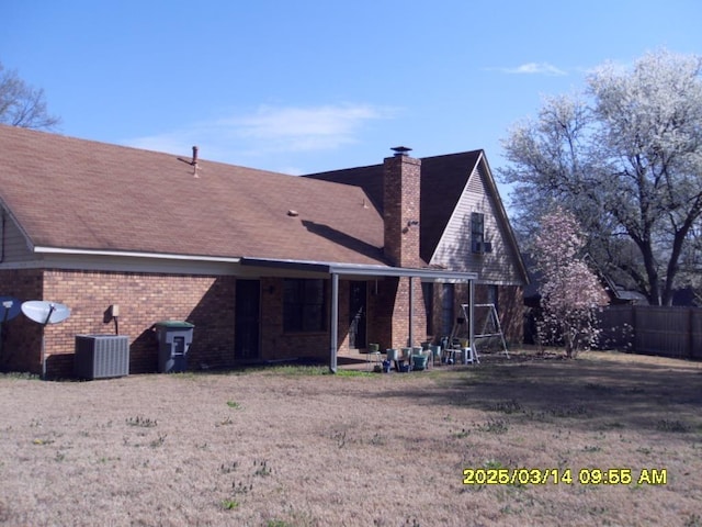 back of house featuring brick siding, a chimney, central AC, and fence