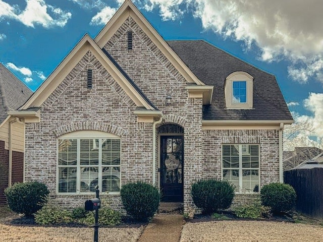 french country home with brick siding, a shingled roof, and fence