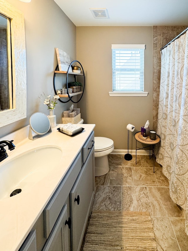 bathroom featuring visible vents, baseboards, toilet, stone tile flooring, and vanity