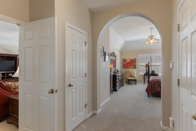 hallway featuring baseboards, arched walkways, lofted ceiling, and light carpet