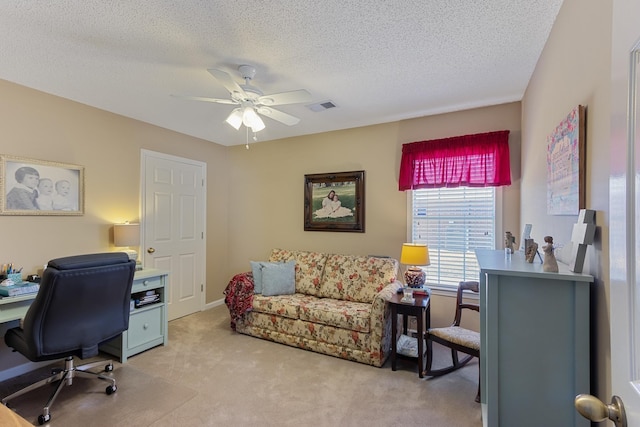 office featuring a textured ceiling, a ceiling fan, visible vents, and light carpet